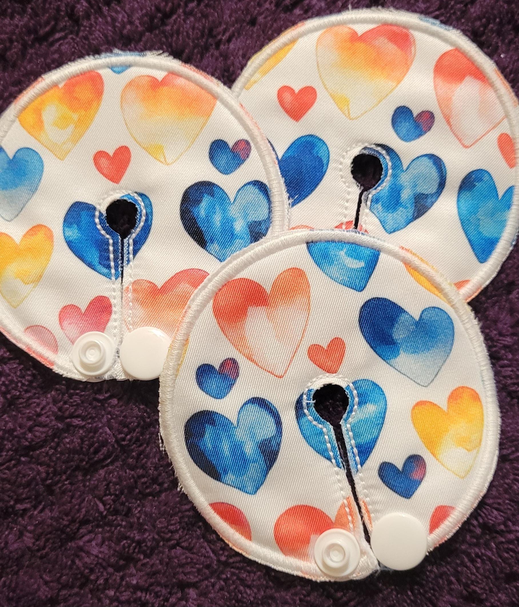 Three round fabric pads with colorful heart patterns on a purple textured background