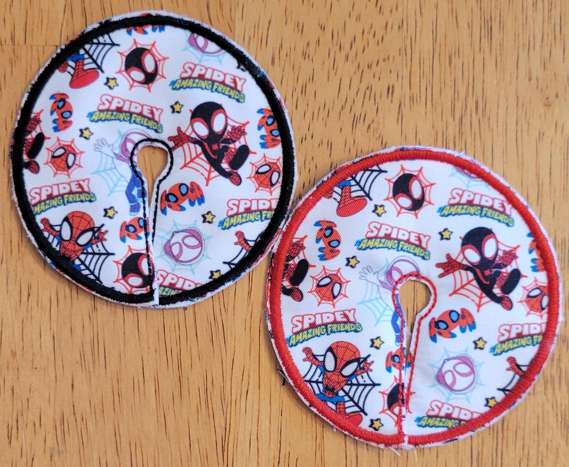 Two round Spider-Man themed coasters on a wooden surface