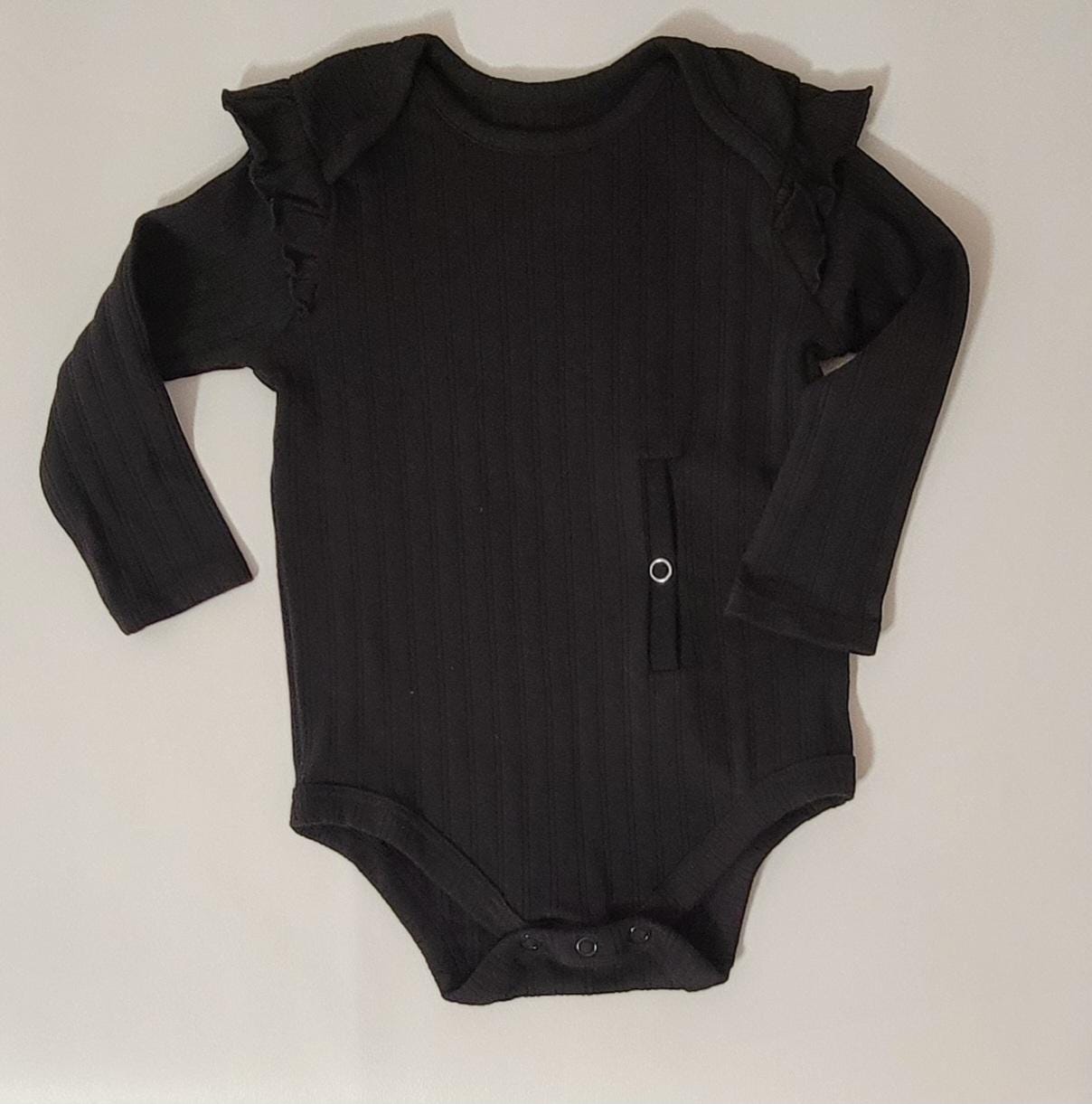 Black baby onesie with ruffled shoulders on a light beige background