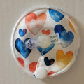 Round fabric pouch with colorful heart patterns and a clear valve on a beige background