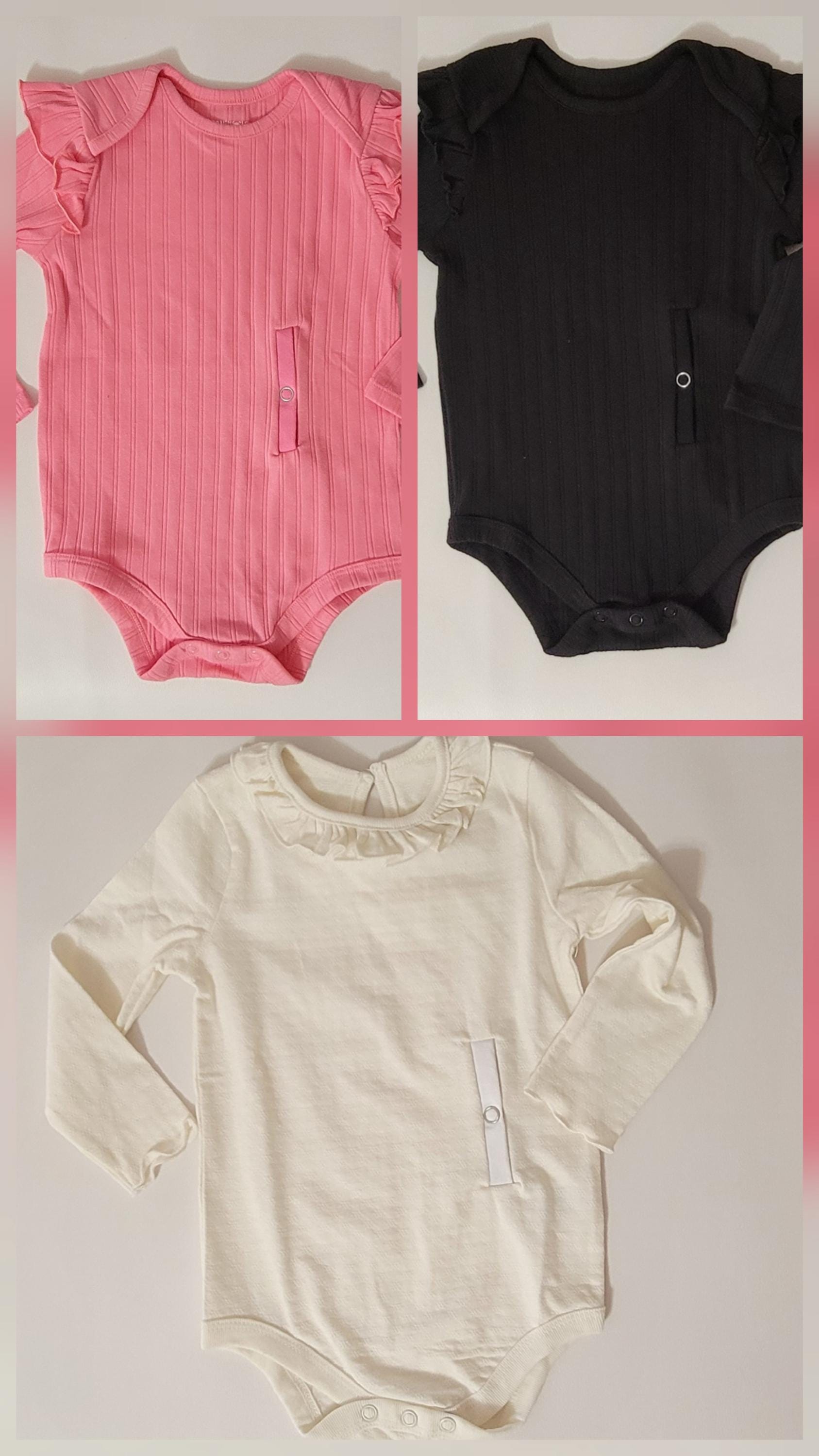 Three baby bodysuits in pink, black, and beige on a pink background.