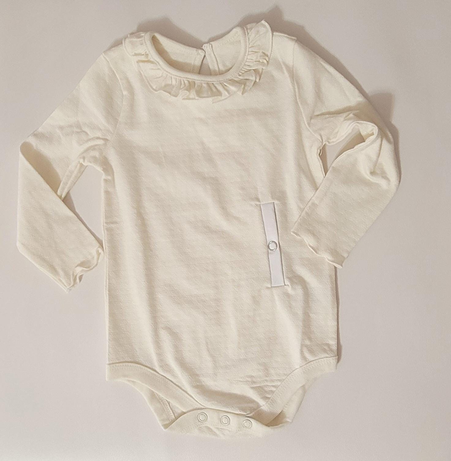 Beige baby onesie with ruffled collar on a light gray background