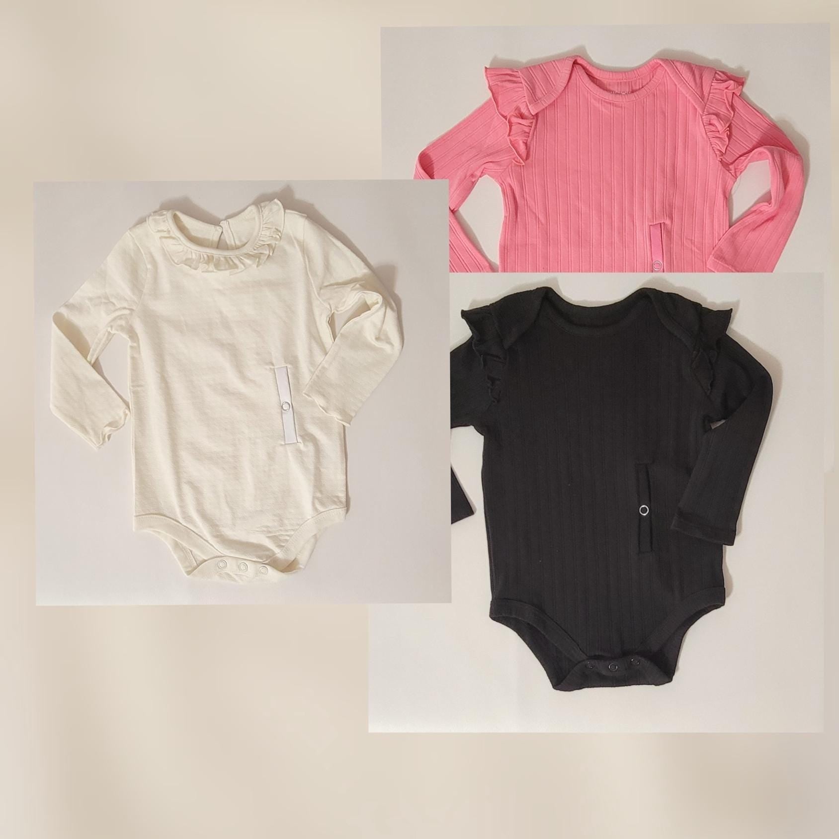 Three baby onesies in pink, black, and white on a light beige background