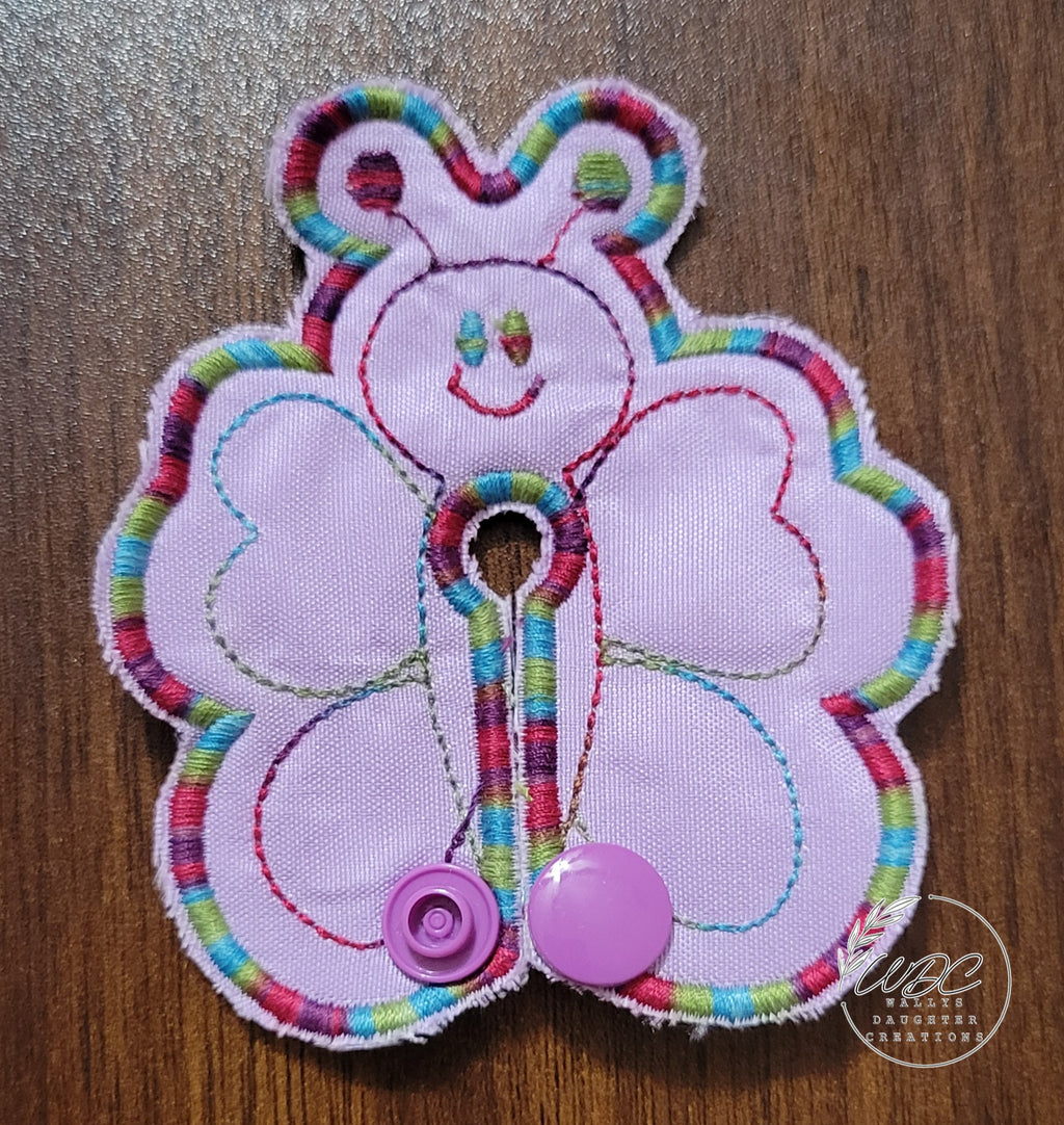 Butterfly shaped gtube pad with multicolored thread on a light purple backgroud.