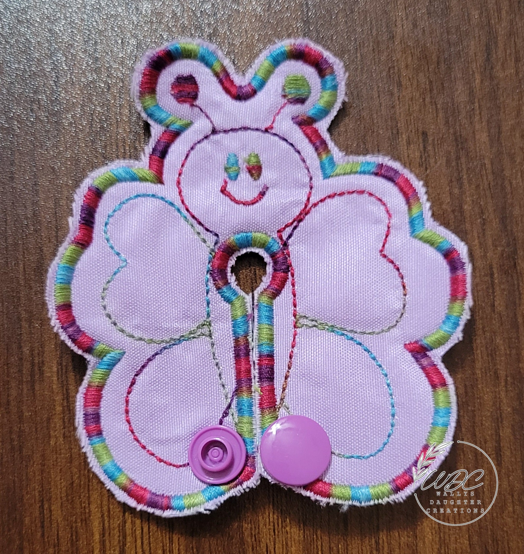 Butterfly shaped gtube pad with multicolored thread on a light purple backgroud.